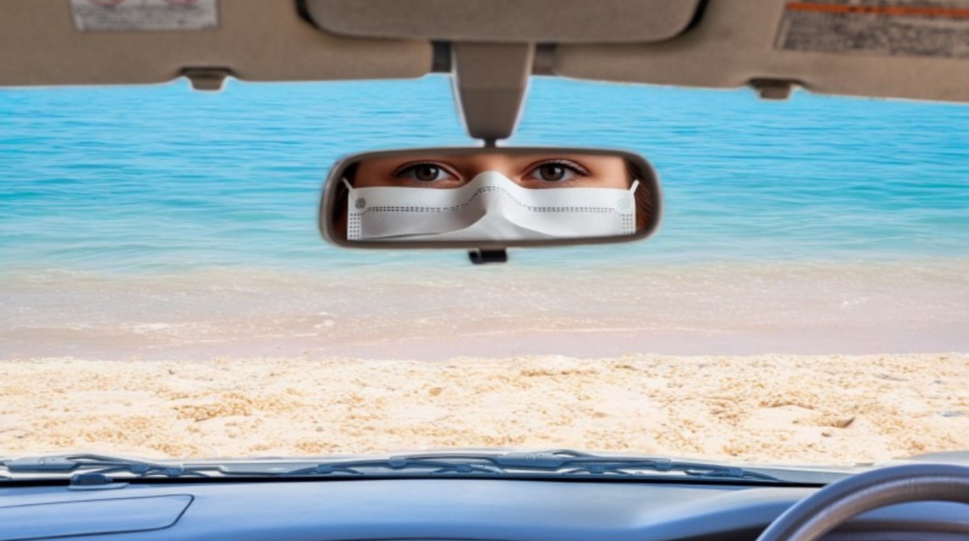 face of female wearing COVID mask seen in middle rearview mirror of car